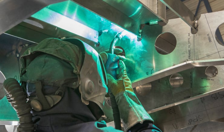 Worker in protective gear welding metal components inside a ship structure.