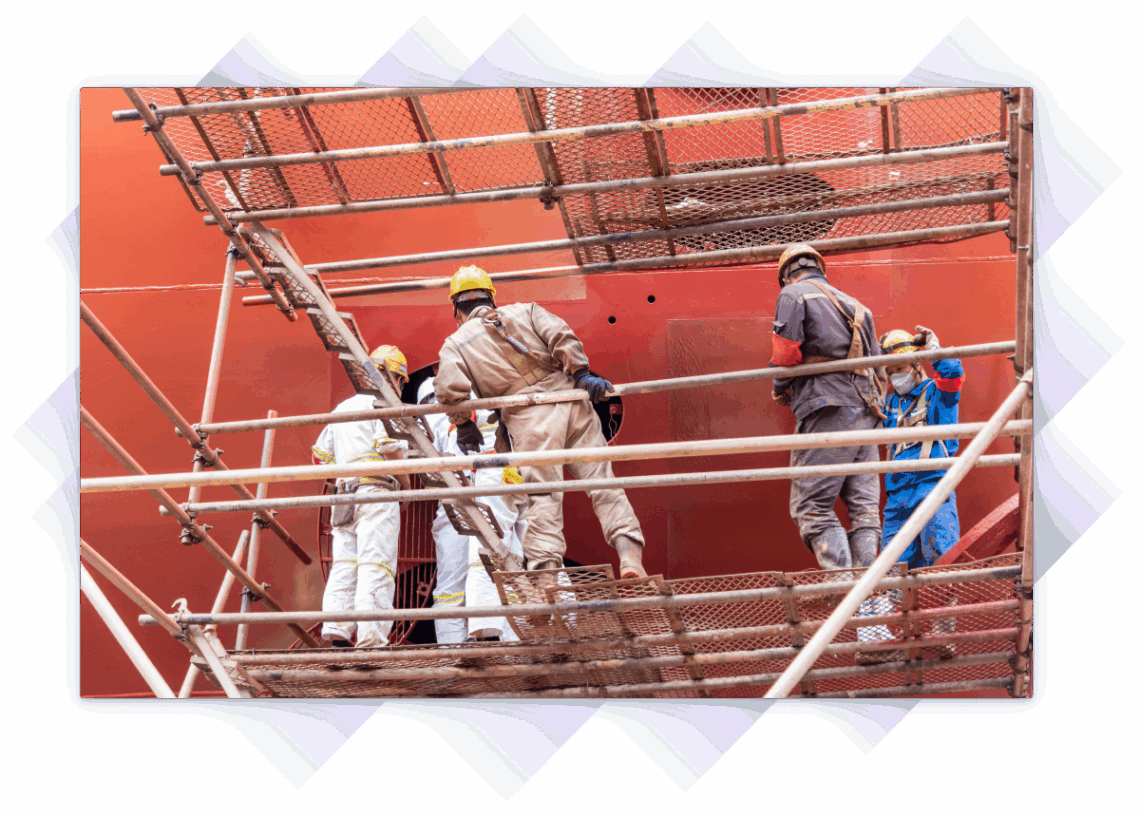 Shipyard crew in safety gear working on scaffolding beside a large vessel.