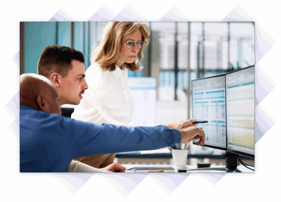 Three professionals review training data on dual monitors in a modern office.