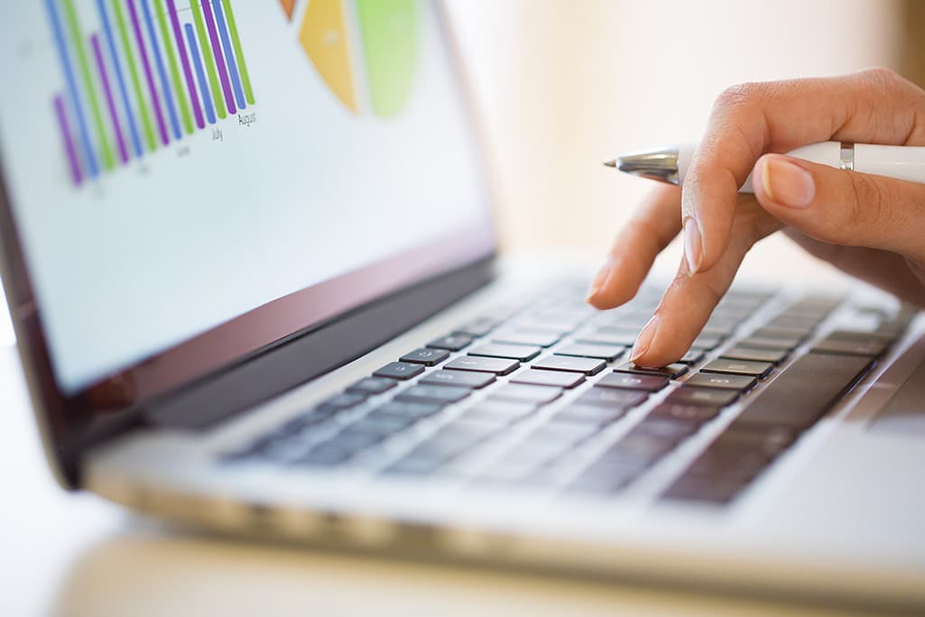 Woman typing on a laptop that has data tables on the screen.