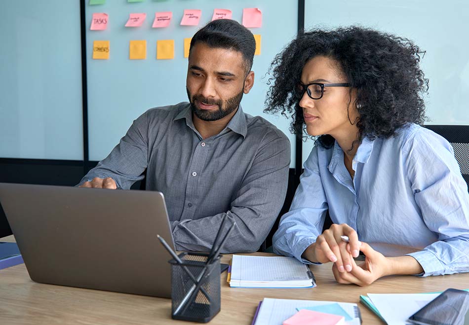 Man and woman pensively planning while man points at a laptop.