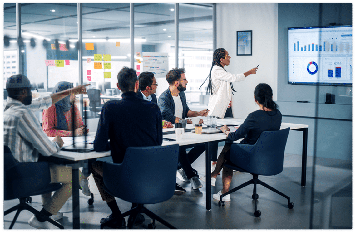 Team meeting in a modern office with a woman gesturing at a screen that has charts with a clicker.