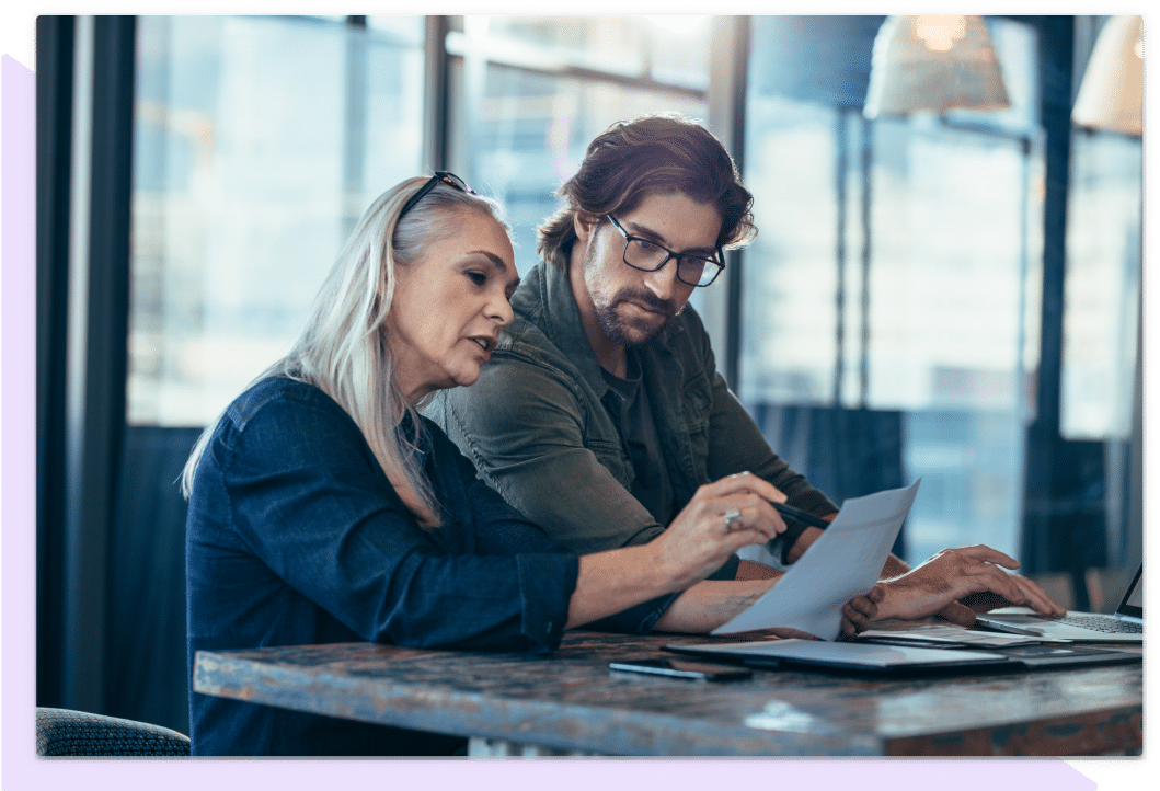 Woman sitting with a man, pointing at details on a document with her pen