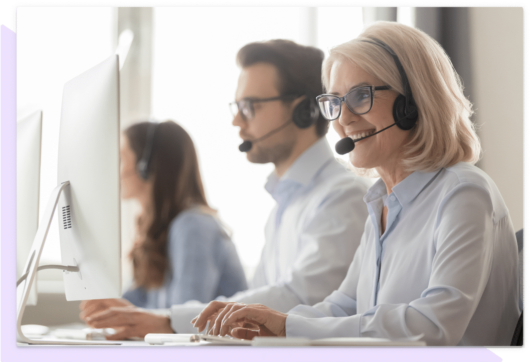 Office workers smiling and talking on telephone headsets.