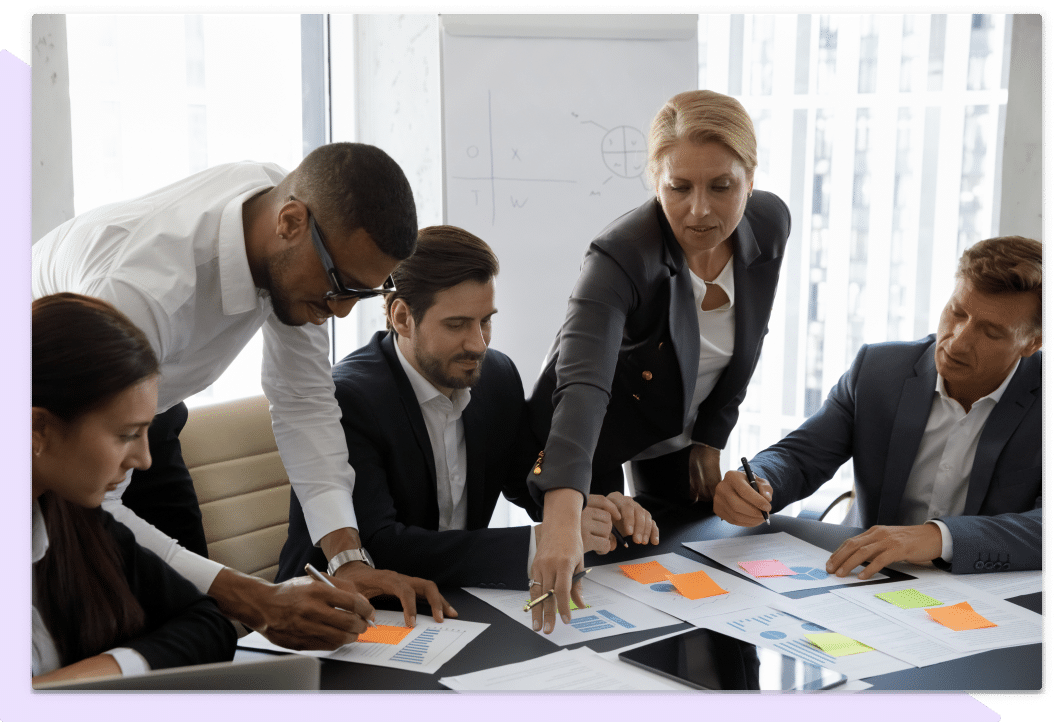 Five training professionals solve problems at a desk, one is reaching for a sticky note to organize their work.