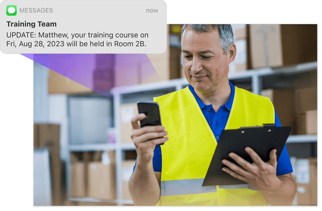 Man in yellow safety jacket with clip board and phone checks a message, a graphic overlay showing an automated training team update SMS from Administrate appears to left of image.