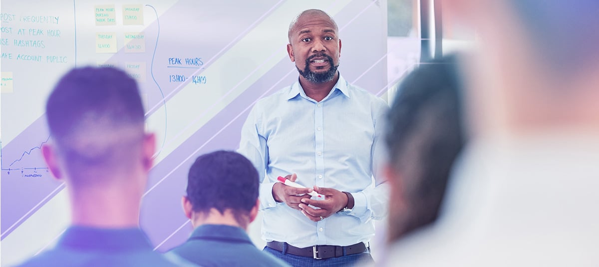 A presenter addresses a group of people using a whiteboard.