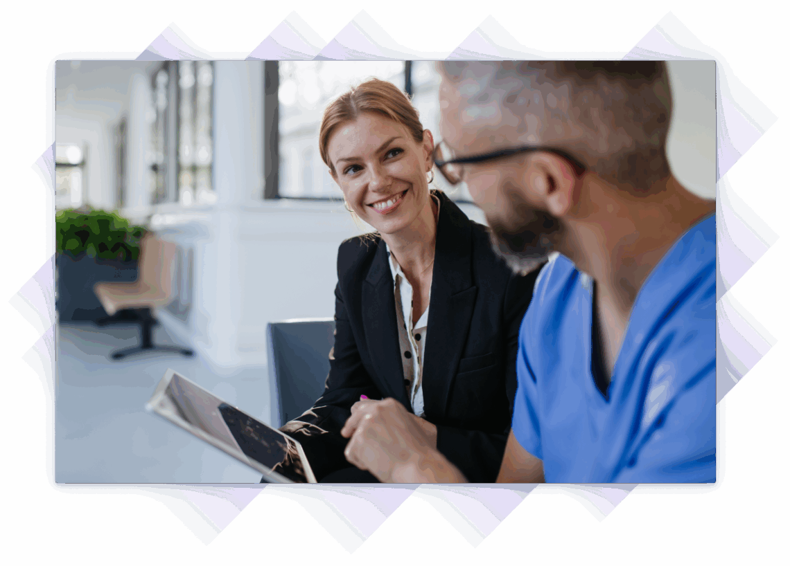 Smiling salesperson discussing something on a tablet with a medical worker in scrubs.