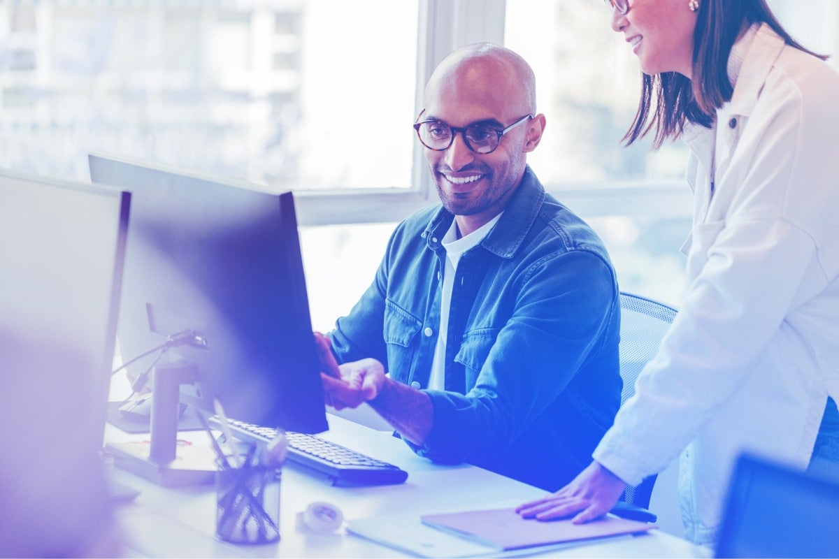 Training professionals consulting a report at a computer monitor, smiling.