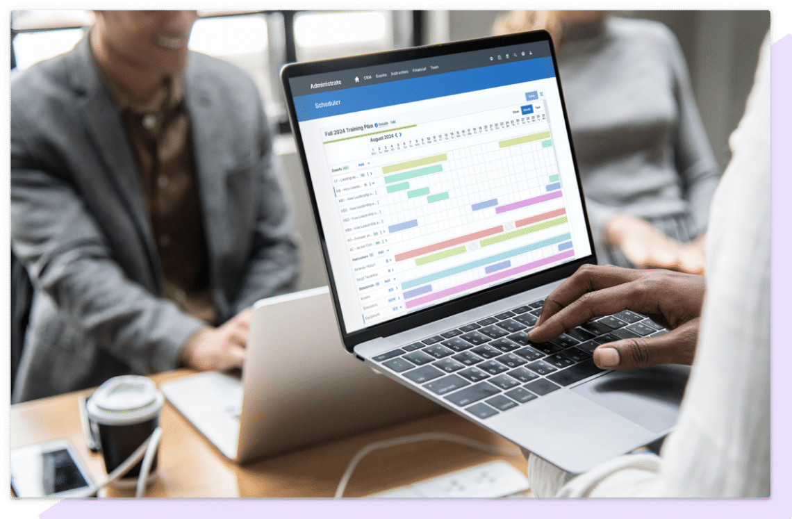 A screenshot of Administrate’s Scheduler on a laptop being held by a training manager, the tool is using AI-powered software to solve a complex training plan.