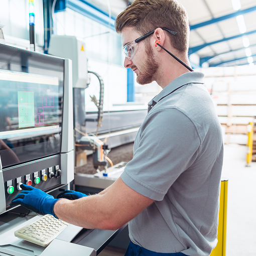 A factory worker operates a control panel on industrial machinery while wearing safety goggles and gloves.