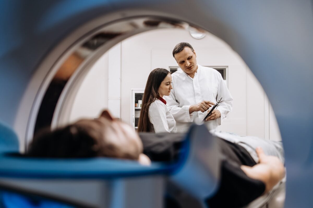 A doctor completes an MRI examination while engaging with a younger doctor.