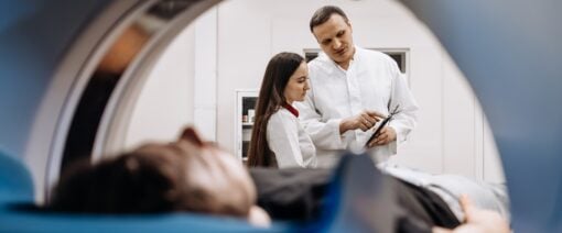 A doctor completes an MRI examination while engaging with a younger doctor.