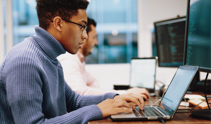 Focused professionals working at laptops and desktop monitors in a modern office, analyzing code or technical data.