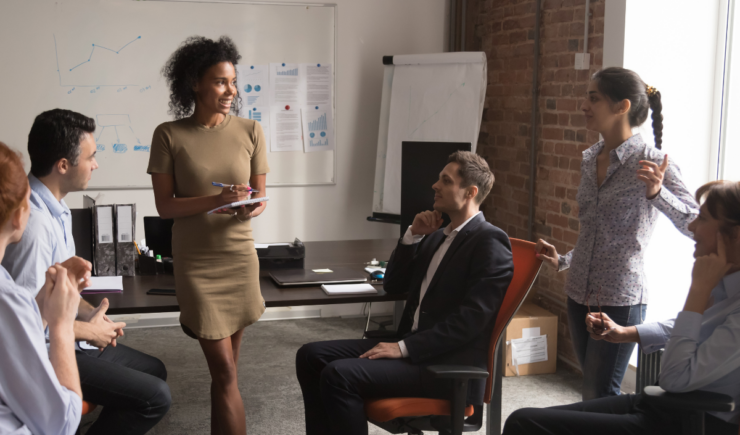 Smiling woman leading a casual office meeting with diverse team members, discussing charts and data in a modern conference room.