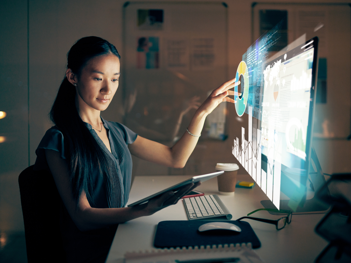 Woman analyzing data visualizations related to enterprise training success stories on a futuristic touchscreen, holding a tablet in a dark office.