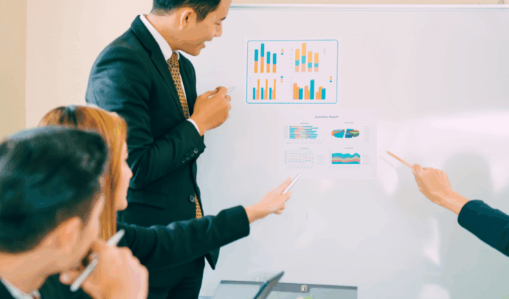 Training professionals discuss charts and analysis of training communication effectiveness, a hand points to a colorful pie chart while a man smiles