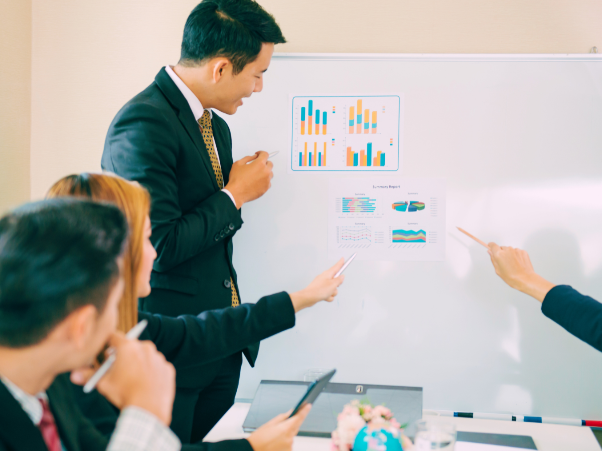 Training professionals discuss charts and analysis of training communication effectiveness, a hand points to a colorful pie chart while a man smiles