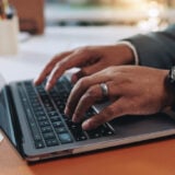Business person with watch typing on a laptop in his office.