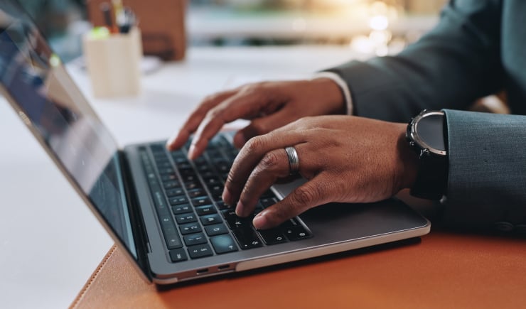 Business person with watch typing on a laptop in his office.