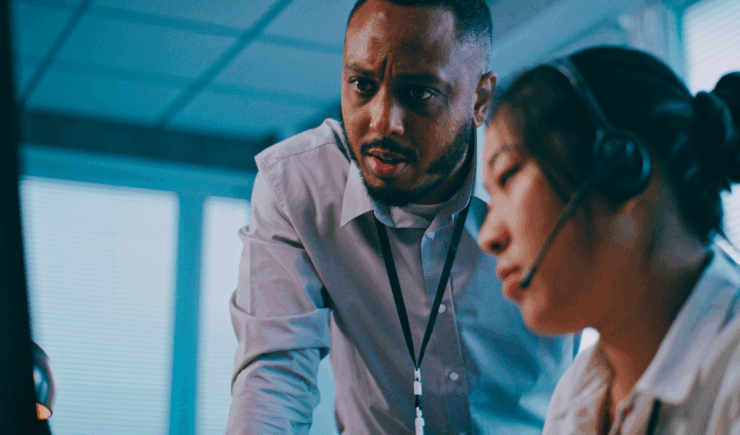 Supervisor at a distributed training firm looking over the shoulder of one of his colleagues with concern.