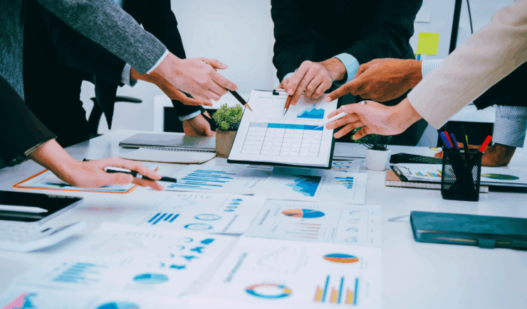 five hands pointing with pens at a clipboard