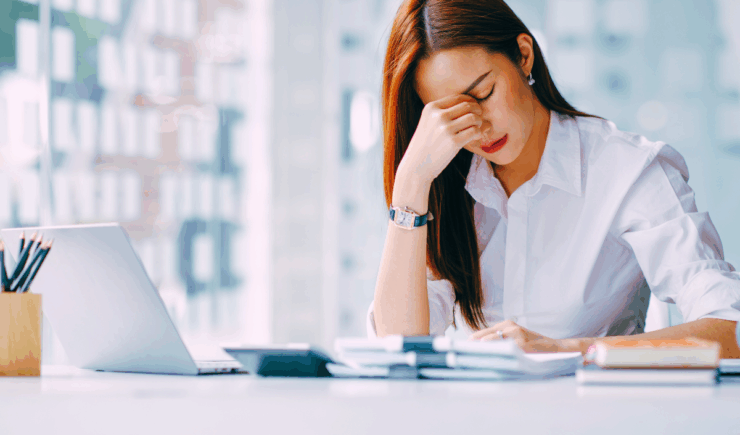 stressed woman at desk holding her nose